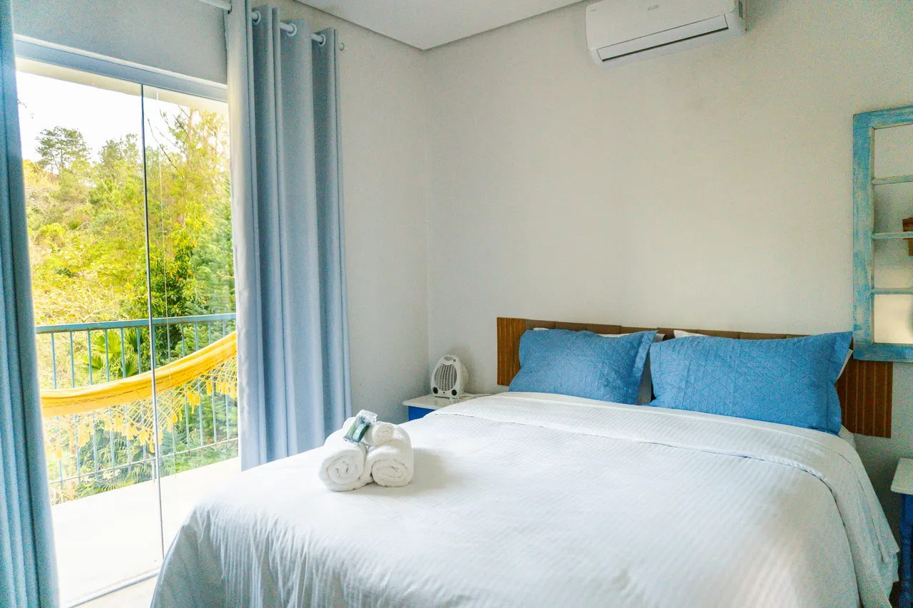 Cama de casal com almofadas azuis e vista verde